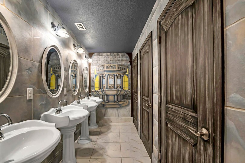 Step inside the lavatory which features 3 bathroom stalls, 3 walk in showers with glass doors and 4 separate vanities